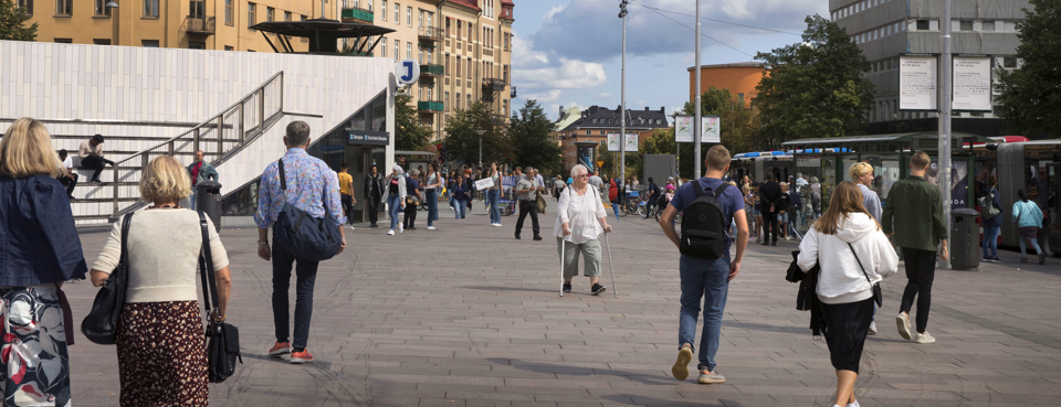 Människor går över ett torg i stadsmiljö. 